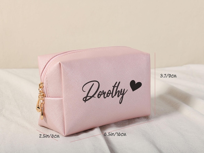 Puede incluir: Una bolsa de cosm&eacute;ticos rosa con una cremallera dorada y el nombre "Dorothy" impreso en negro con un peque&ntilde;o coraz&oacute;n negro. La bolsa mide 16 cm por 9 cm.