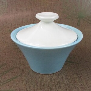 May include: A light blue ceramic sugar bowl with a white lid. The bowl has a rounded shape and a smooth, glossy finish.