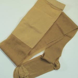 May include: A pair of tan-coloured pantyhose, displayed flat against a white backdrop. The pantyhose feature a reinforced toe and a darker band at the top. The material appears sheer and lightweight.