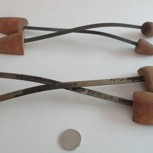 May include: Two pairs of wooden shoe trees with metal spring mechanisms. The shoe trees are brown and the metal is silver.
