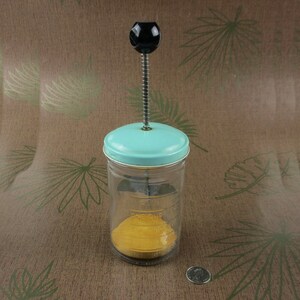 Peut inclure: Un moulin à légumes vintage bleu et blanc avec une manivelle et un pot en verre avec des mesures. Le pot est rempli d'une substance jaune.