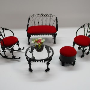 May include: A miniature dollhouse furniture set featuring a black metal loveseat, a rocking chair, a standard chair, and a round stool, all with bright red velvet cushions. A small round glass-topped table holds a tiny bouquet of colourful flowers.