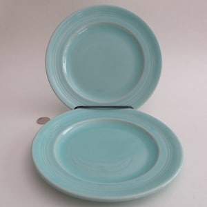 May include: Two light blue ceramic salad plates with a raised rim and a subtle ribbing pattern.