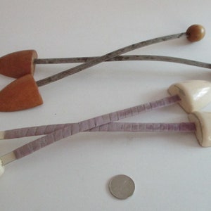 May include: Two pairs of shoe trees. One pair is made of light brown wood with metal and wooden knobs. The other pair is off-white with a lavender fabric and metal. A coin is in the foreground.