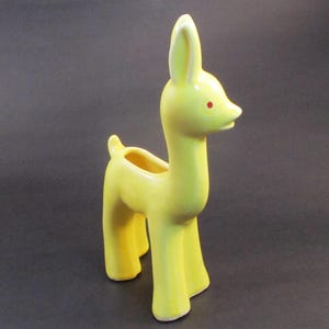 May include: A yellow ceramic planter shaped like a deer with red eyes. The planter has a small opening on the back for planting.