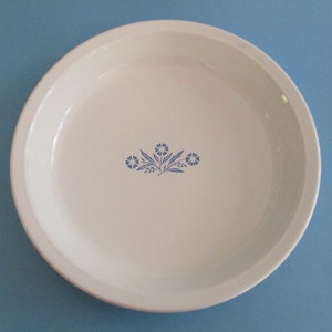 May include: White pie dish with a blue floral design. The design features three stylised flowers with leaves.