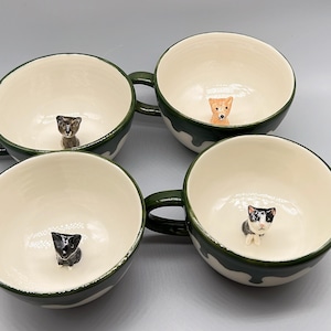 May include: Four ceramic mugs with green and white designs. Each mug features a small figurine of a cat or dog inside.