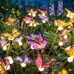 May include: A collection of solar-powered garden stakes featuring artificial butterflies in shades of orange, purple, and pink. Each butterfly is mounted on a thin metal stem with a small, glowing white LED light positioned directly beneath the wings.