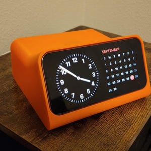 May include: An orange digital clock with a black screen displaying the time and a calendar for September. The clock has a rectangular shape with rounded edges and is sitting on a wooden surface.