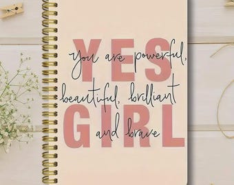 May include: A spiral-bound notebook with a cream-colored cover. The cover features the words "YES GIRL" in large pink letters, with the phrases "you are powerful, beautiful, brilliant and brave" in black script.