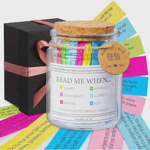 May include: A glass jar with a cork lid filled with colourful Bible verses, labelled "Read Me When..." and "Color Coded Bible Verses." A gift box with a pink ribbon sits beside the jar. A small tag reads "For You."