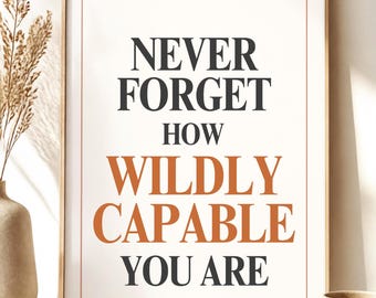May include: A rectangular wall art print in a wooden frame featuring the text NEVER FORGET HOW WILDLY CAPABLE YOU ARE. The words NEVER FORGET, HOW, and YOU ARE are in black, while WILDLY CAPABLE is in orange. A thin orange border surrounds the text.