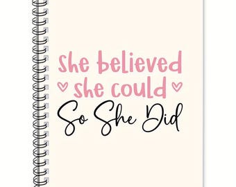 May include: A spiral-bound notebook with a cream-colored cover. The cover features the text "she believed she could" in pink, with hearts, and "So She Did" in black script.