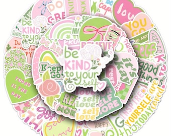May include: A collection of stickers in a circular arrangement, featuring various designs in shades of pink, green, and white. The stickers display inspirational quotes and phrases such as "Be Kind to Yourself," "Today is the Day," and "Love."