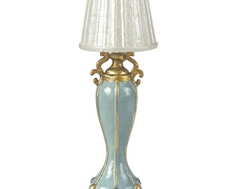 Op de afbeelding: Een miniatuur decoratieve lamp met een lichtblauwe basis en gouden details. De lamp heeft een witte lampenkap. Het ontwerp is sierlijk en elegant, geschikt voor decoratief gebruik. Het is een klein, decoratief item.