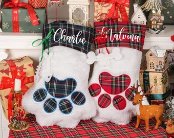 May include: Two white Christmas stockings with paw print designs. One has a green and blue plaid paw print and the name "Charlie". The other has a red plaid paw print and the name "Malvina". Both have plaid tops.