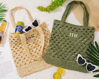 May include: Two crochet tote bags, one beige and one olive green, with openwork designs. The beige bag has the initials "ASR" and the green bag has "HR". Both bags have handles and are filled with items like sunglasses and a beverage.