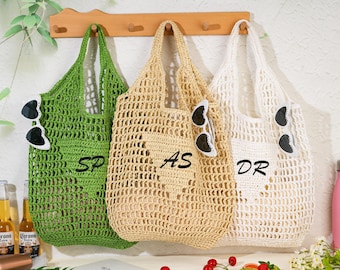 May include: Three crocheted tote bags hanging on a wooden rack. The bags are green, beige, and white. Each bag has a different letter initial on it: SP, AS, and DR.