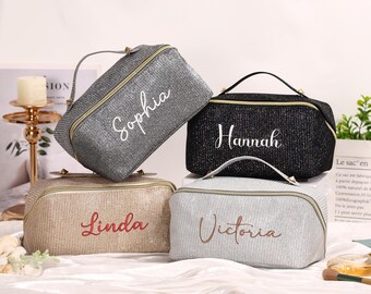 May include: Four glitter cosmetic bags in silver, black, gold, and light gray, each with a different name embroidered on the front: Sophia, Hannah, Linda, and Victoria. The bags have a handle and a zipper closure.