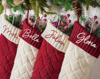May include: Four personalized Christmas stockings in red and cream, each with a name embroidered in a cursive font. The stockings are decorated with candy canes, berries, and greenery, creating a festive holiday display.