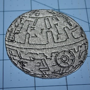 May include: A silver and black embroidered patch of the Death Star from Star Wars.