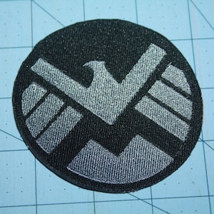 May include: A black and silver embroidered patch featuring the S.H.I.E.L.D. logo.