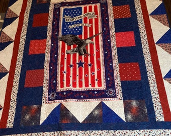 May include: A red, white, and blue patriotic quilt with a bald eagle and the words "Liberty and Justice for All" on a banner. The quilt is made of various fabrics with stars and stripes patterns.