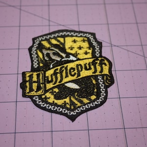 May include: A yellow and black embroidered patch with a badger and the words "Hufflepuff" in a banner.