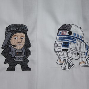 May include: Embroidered patch featuring a cartoon image of a Star Wars character, Darth Vader, and a robot, R2-D2.