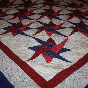 May include: A quilt with a red, white, and blue star pattern. The quilt is made of fabric with a small white polka dot pattern. The quilt is edged with a red and white border.