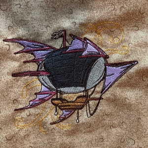 May include: Embroidered design of a purple and black airship with a gold gondola. The airship has wings and is surrounded by gold swirls.