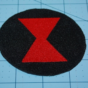May include: A black circle patch with a red hourglass shape in the center.