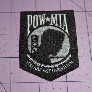 May include: Black and white embroidered patch with the words "POW*MIA" and a silhouette of a soldier's head. The text below the silhouette reads "You Are Not Forgotten."