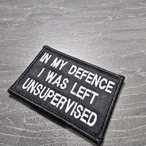 May include: Black fabric patch with white text that reads "In my defence I was left unsupervised".
