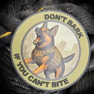 May include: A circular patch featuring a German Shepherd illustration in a tactical vest with an American flag. The text around the edge reads "DON'T BARK IF YOU CAN'T BITE."