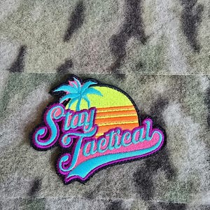 May include: A black and purple embroidered patch with a palm tree and sunset graphic. The text "Stay Tactical" is in a blue and pink font.