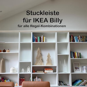 Könnte beinhalten: Weißer Einbauschrank mit mehreren Regalen, gefüllt mit Büchern, Dekorationsartikeln und gerahmten Bildern. Der Text an der Wand lautet "Stuckleiste für IKEA Billy für alle Regal-Kombinationen."