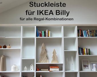 May include: White built-in bookcase with multiple shelves, filled with books, decorative items, and framed pictures. The text on the wall reads "Stuckleiste für IKEA Billy für alle Regal-Kombinationen."