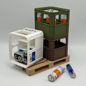 Könnte beinhalten: Ein Miniatur-Kunststoffbehälter in Weiß mit dem Wort "LEER" obenauf, der zwei 9-Volt-Batterien und zwei AA-Batterien enthält. Eine kleine Holzpalette stützt den Behälter. Zwei gestapelte grüne und braune Kisten enthalten AA-Batterien. Zwei AA-Batterien liegen auf der Oberfläche.