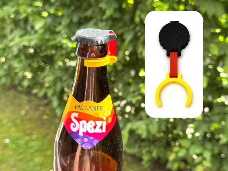 K&ouml;nnte beinhalten: Ein Flaschen&ouml;ffner-Aufsatz mit einem schwarzen runden Oberteil, einem roten vertikalen Verbindungsst&uuml;ck und einem gelben Ringfu&szlig;. Das Ger&auml;t ist am Hals einer braunen Glasflasche mit dem bunten Etikett Paulaner Spezi befestigt.