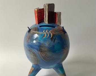 A ceramic book-themed money box that is also a small work of art. It is blue in color and measures 24 cm high and 14 cm wide.