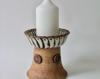 A candle holder or stand for pillar candles made of densely fired stoneware clay in cream color with black and white decoration.
