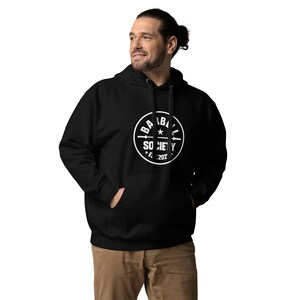 May include: Black hoodie with a white circular graphic that reads "BARBELL SOCIETY" with a barbell and star design. The hoodie has a drawstring hood and a front pocket. The text "Est. 2021" is also included in the graphic.