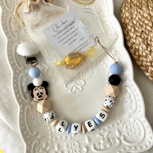 Könnte beinhalten: Ein Schnullerhalter mit einer Mickey-Maus-Perle, hellblauen, schwarzen, weißen und beigen Silikonperlen sowie weißen Buchstabenperlen, die LYES bilden. Enthält einen kleinen Organzabeutel mit einer Notiz und einem Werther's Original Bonbon.