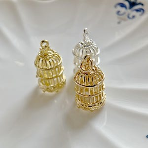 Puede incluir: Tres abalorios de jaula de pájaros dorados, dos con acabado dorado y uno con acabado plateado. Los abalorios están detallados con intrincados diseños de alambre y son perfectos para agregar un toque de fantasía a los proyectos de joyería.