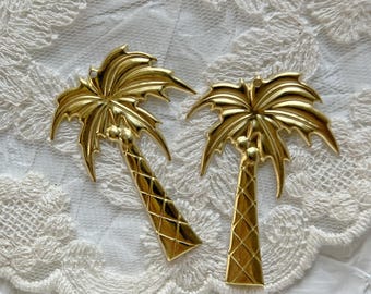 May include: Two gold palm tree ornaments with a diamond pattern on the trunk. The ornaments are on a white lace background.