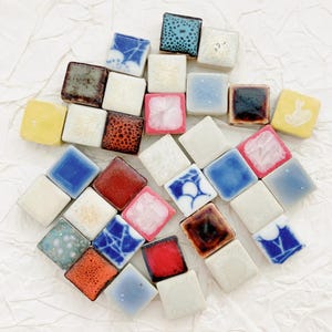 May include: A selection of small, square ceramic tiles in diverse colours and patterns. The tiles have a glossy finish, including shades of blue, red, white, yellow, and brown. Some tiles feature floral or abstract designs.