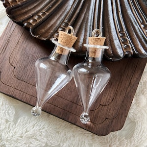 May include: Two clear glass bottles with cork stoppers and silver tops. The bottles are teardrop shaped and have a pointed bottom.