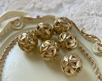 May include: A group of seven gold-colored metal beads with a leaf design. The beads are arranged in a circle on a white surface.