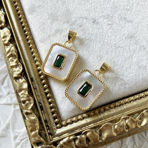 Puede incluir: Dos colgantes de oro con detalles de nácar blanco y piedras preciosas verdes. Los colgantes son de forma cuadrada con un borde decorativo.